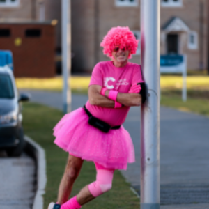 David dressed all in pink, including a pink tutu and a pink curly wig, leaning against a lamppost 