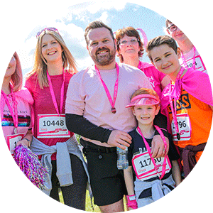 Family of men, women and children all dressed in pink with their medals at Race for Life with paid event staff