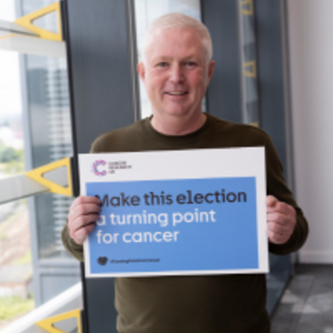 Simon holding a sign that says 'Make this election a turning point for cancer'