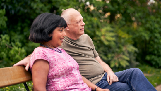 Couple sit outside on a bench with hedge behind them