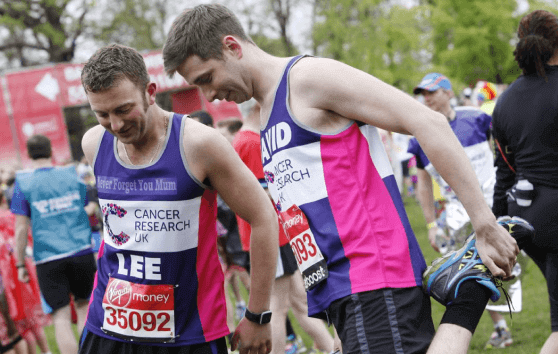 Two runners in Cancer Research UK running vests, stretching before a race 