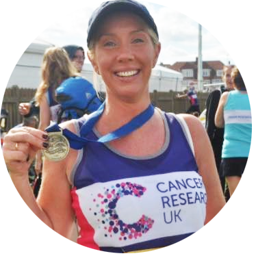 Bridie smiling wearing a CRUK running vest holding her medal 