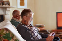 An older lady sat on a sofa reading something on her phone