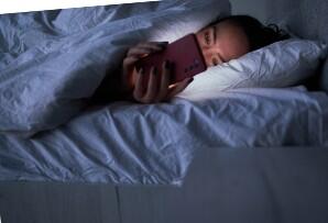 woman laying in bed looking at her phone