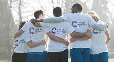 Backs of five people in Cancer Research UK branded t-shirts hugging