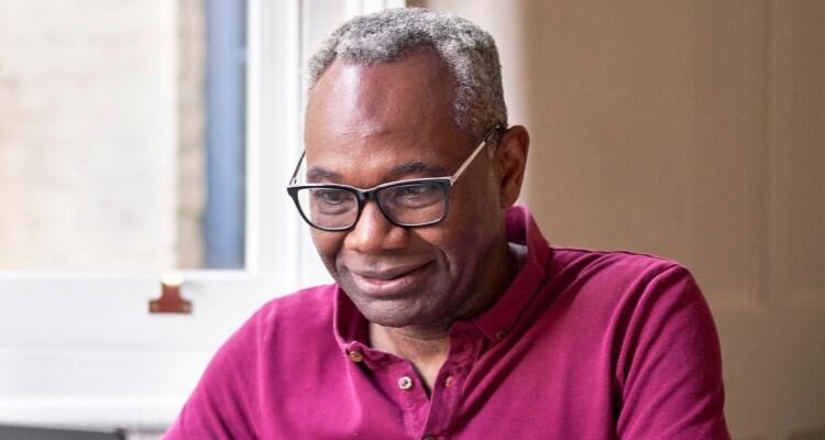 An image of a man in a red shirt sat looking down, partly smiling