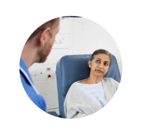 A female cancer patient sat in a chair in hospital talking to a nurse