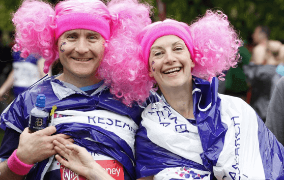 Two individuals smiling wearing pink wigs 