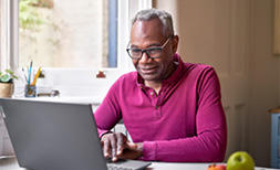 A man using the free will service is sat at his kitchen table on his laptop, updating his will online from the comfort of his home on his own.