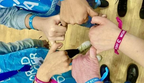 Five hands connected in a circle wearing World Cancer Day wristbands