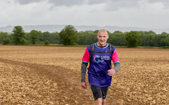 Man hiking in field wearing a Cancer Research UK top