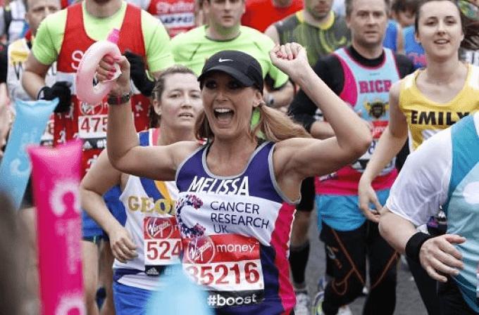 A female runner wearing a CRUK running vest holding her hands in the air during the London Marathon