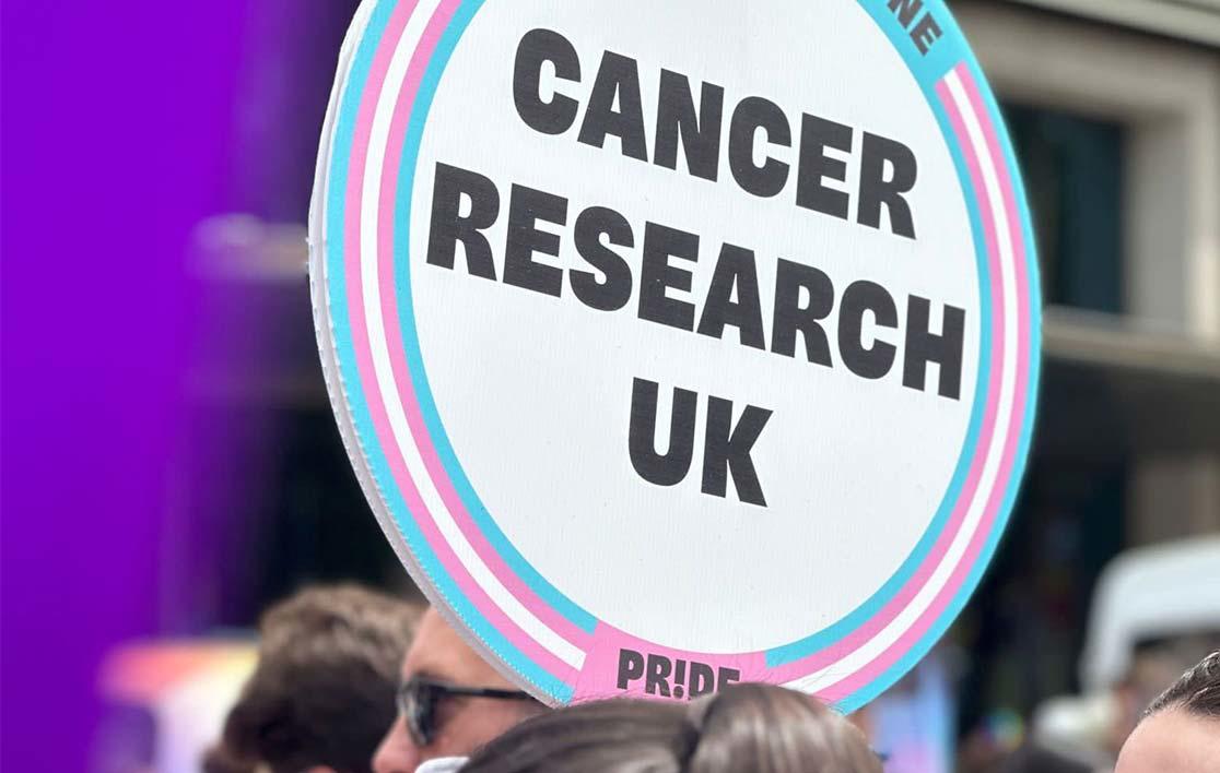 A photo of a person at London Pride 2023 holding a sign that reads Cancer Research UK Pride