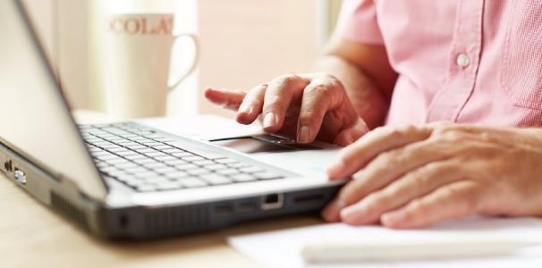 An image of a man's hands typing at a laptop