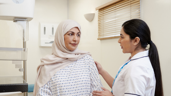 mammographer with a patient, wearing a hospital gown, before a mammogram.
