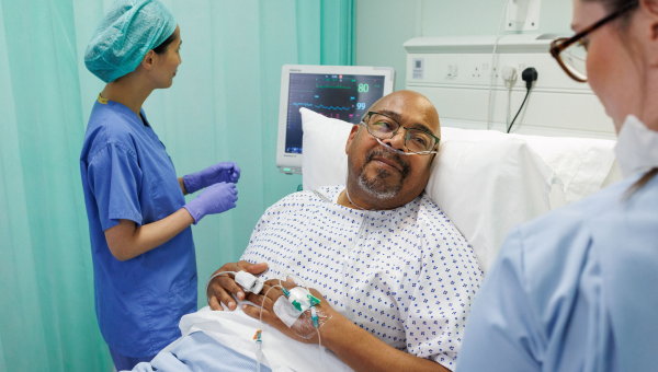 Patient in hospital bed speaking to health professionals who are checking vitals