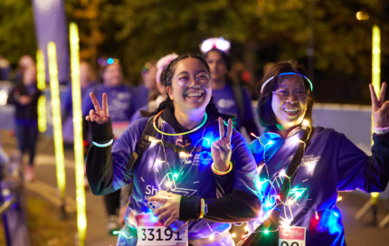 Two female Shine Walk participants walking the course with peace fingers raised and bright leds across their t-shirts