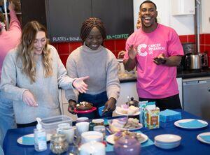 Picture of a coffee morning that shows three people smiling - one wearing a Cancer Research UK t-shirt, mugs and cake