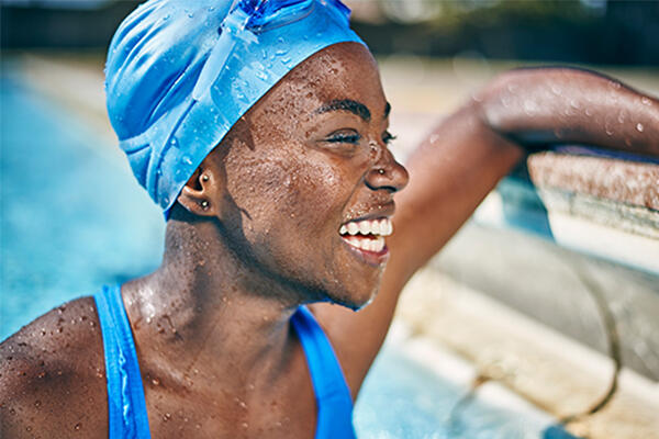 A lady in a blue swim cap rests at the side of the pool