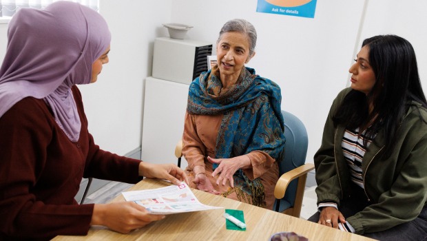 Female Dr sat at a desk showing a leaflet to two woman