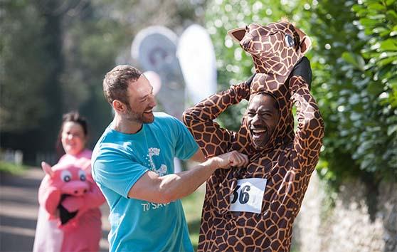 Photo of a CRUK staff member helping a fundraiser zip up their giraffe costume