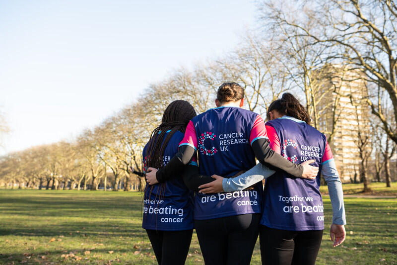 3 people hugging each other wearing the Cancer Research UK running tops